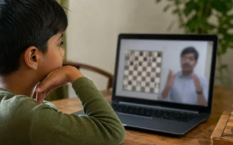 Indian child in a quiet home corner on a laptop video chess lesson beside a wooden set — ChessWize