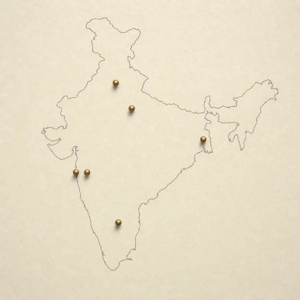 Hand-drawn outline map of India with brass-colored pins at coach-served cities including Bengaluru, Pune, Kolkata, Kanpur, Delhi, and Mumbai
